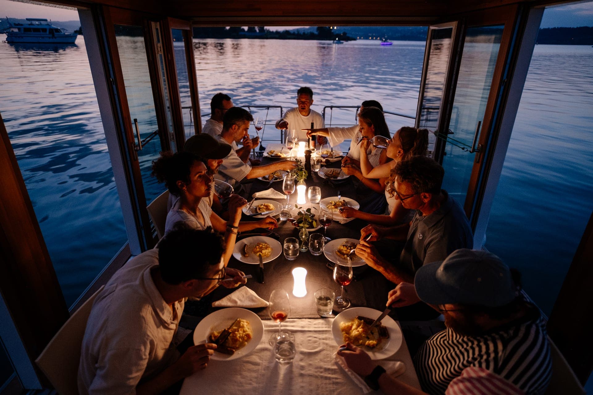 Gäste beim Dinner an Bord des Eventflosses mit geöffneter Fensterfront zum Zürichsee